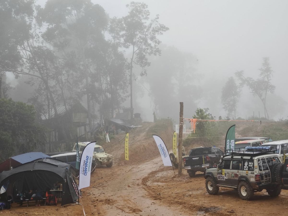 Kenderaan pacuan empat roda peserta di denai hutan berkabus yang dipenuhi bendera PETRONAS Dynamic Diesel