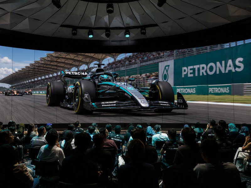 A crowd watching a Mercedes-AMG PETRONAS F1 car on a large screen at a live race viewing event